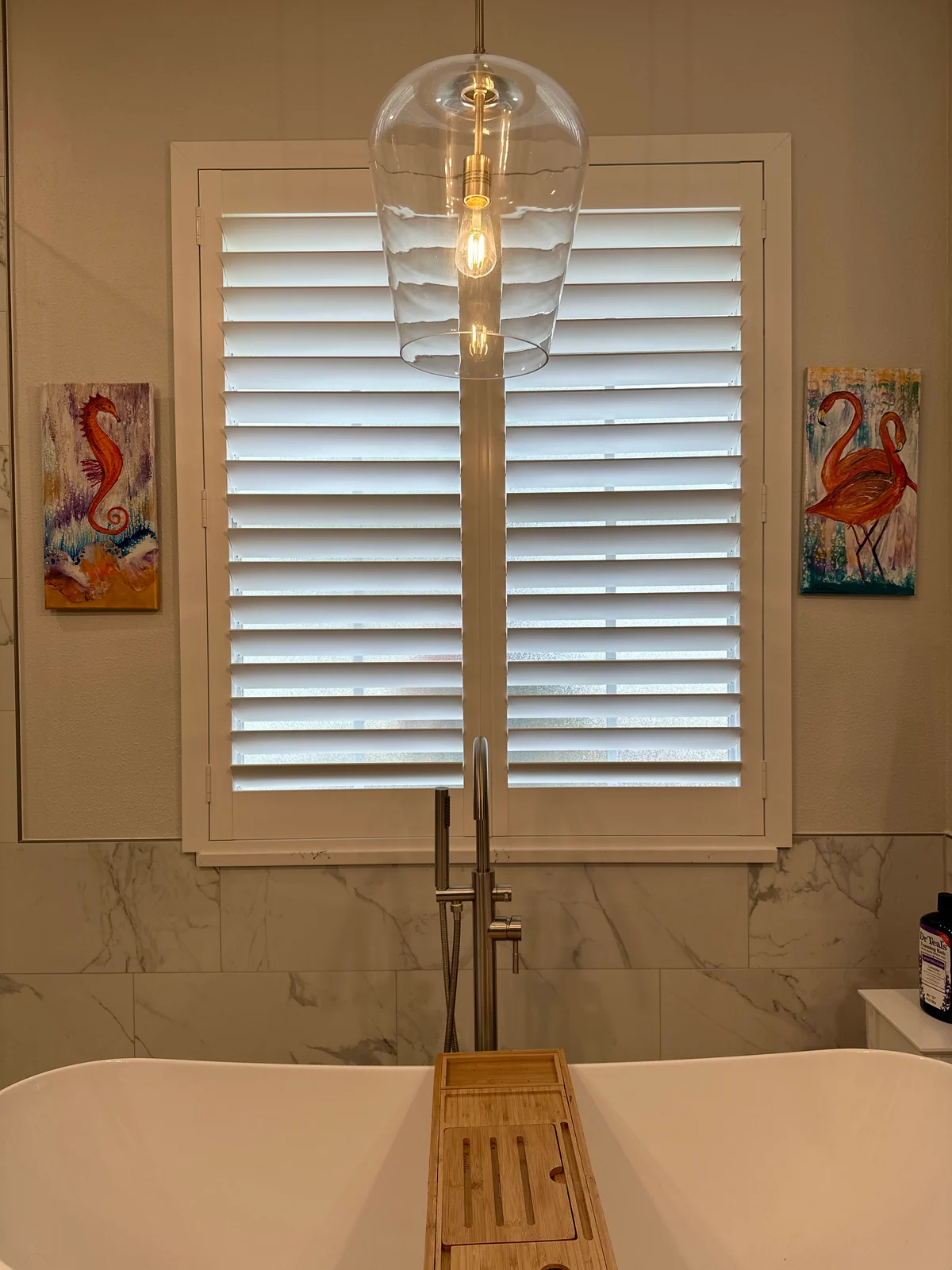 White plantation shutters on a bathroom window behind a glass pendant light