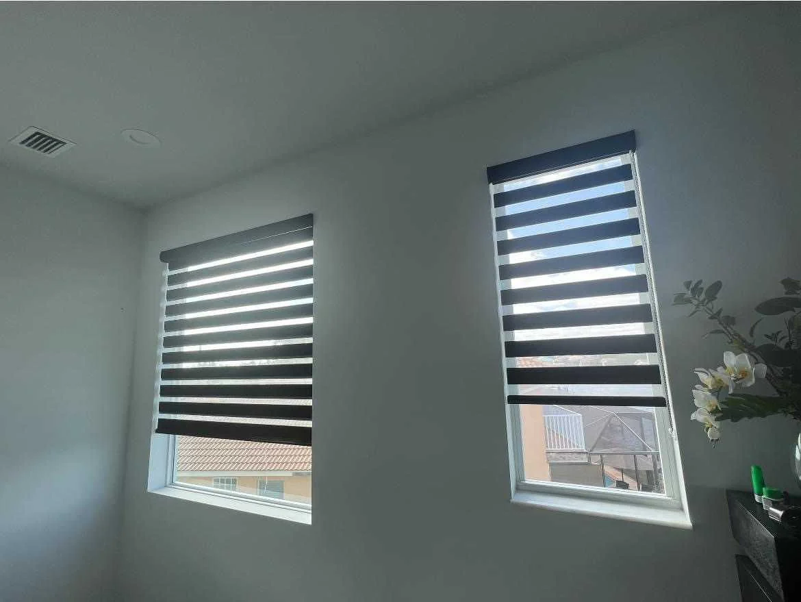Dark layered shades with sheer bands filtering daylight through two tall windows