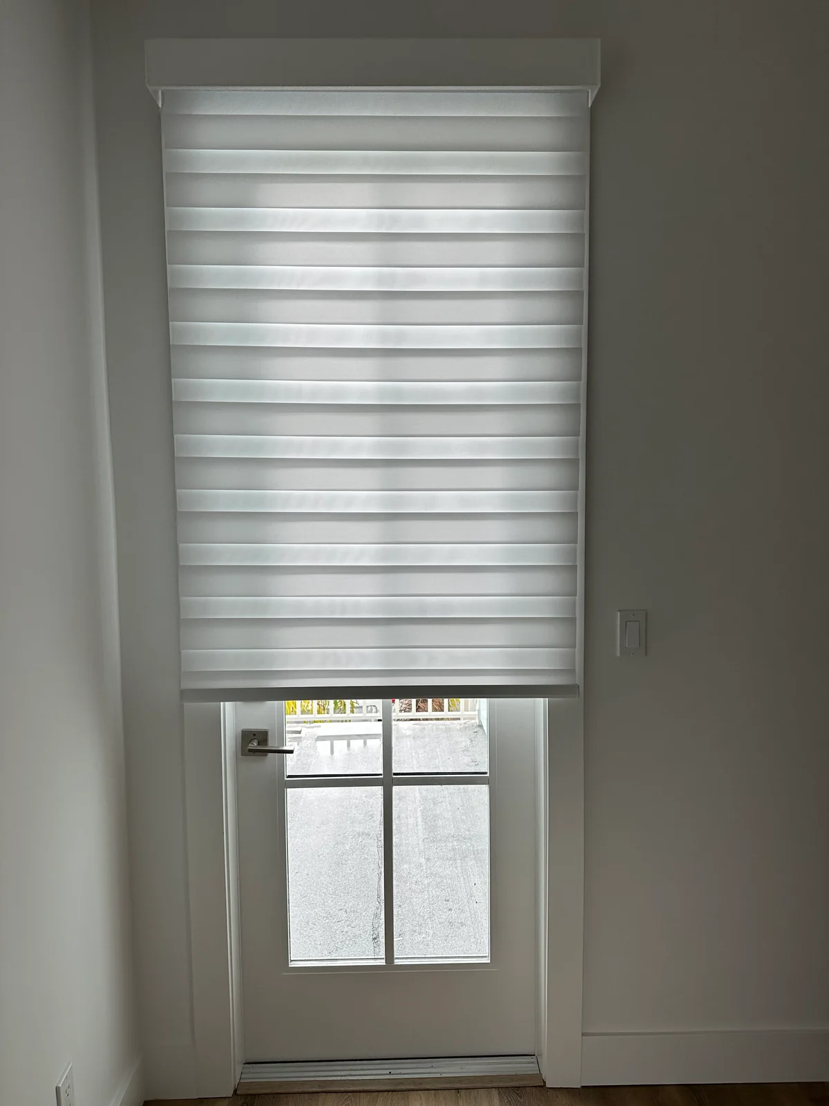 White layered shade with alternating fabric bands fitted above a glass door